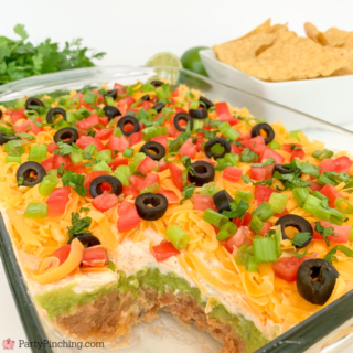 The best layered taco dip, easy best taco dip recipe, hot or cold taco dip recipe, easy appetizer dip for big game superbowl, best picnic potluck ideas for a crowd easy family friendly budget meals, beans guacamole sour cream taco seasoning tomato onion cheese olives lime taco dip